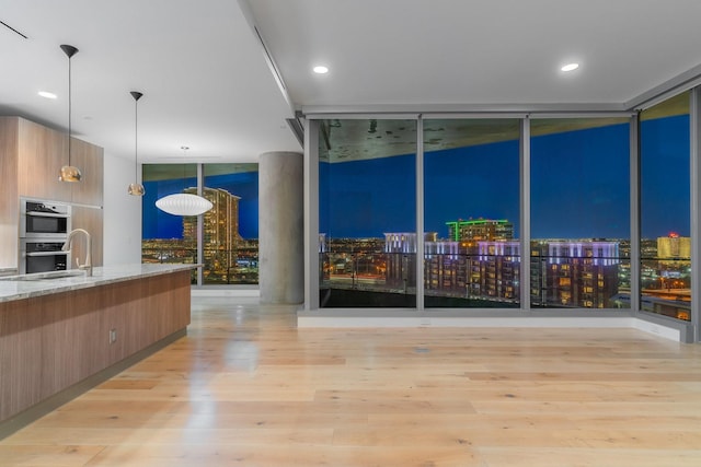 kitchen featuring a wall of windows, modern cabinets, stainless steel double oven, a sink, and light wood-type flooring