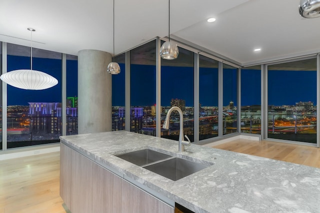 kitchen featuring floor to ceiling windows, a sink, pendant lighting, light stone countertops, and wood finished floors