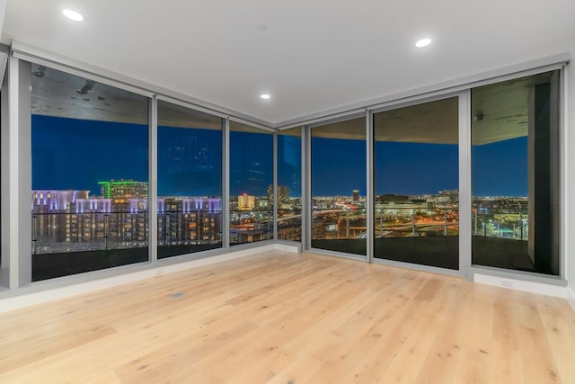 empty room featuring expansive windows, a view of city lights, and wood finished floors