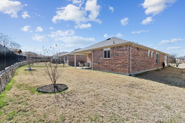 exterior space with a fenced backyard, brick siding, a patio area, a lawn, and a shingled roof