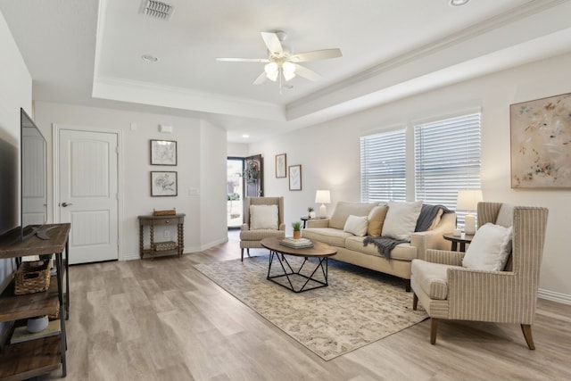 living room with a raised ceiling, light wood-style flooring, visible vents, and a ceiling fan