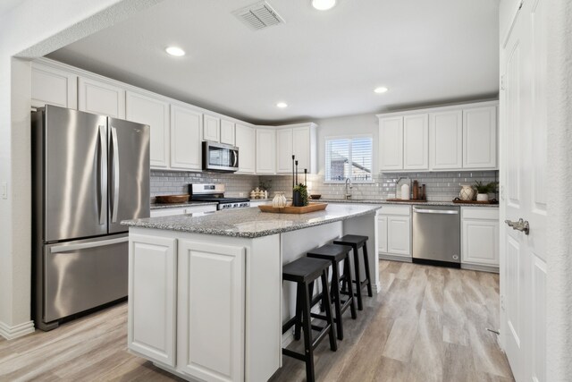 kitchen featuring tasteful backsplash, stainless steel appliances, light wood finished floors, white cabinetry, and visible vents