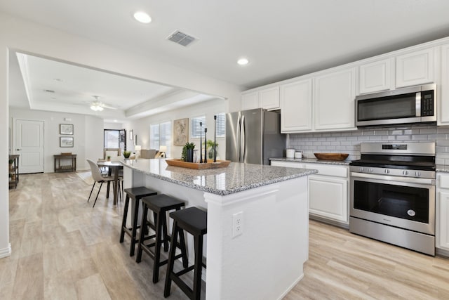 kitchen featuring decorative backsplash, a tray ceiling, white cabinets, appliances with stainless steel finishes, and visible vents