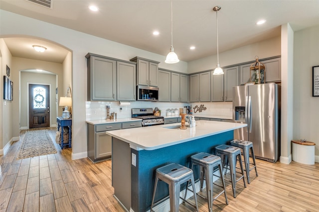 kitchen with gray cabinets, arched walkways, a sink, stainless steel appliances, and a kitchen breakfast bar