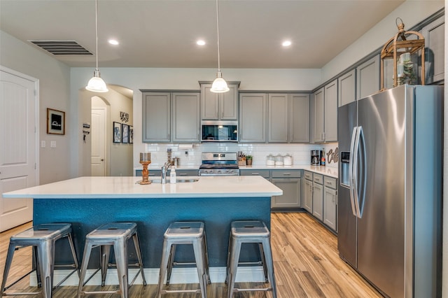 kitchen with visible vents, arched walkways, gray cabinetry, stainless steel appliances, and a kitchen breakfast bar