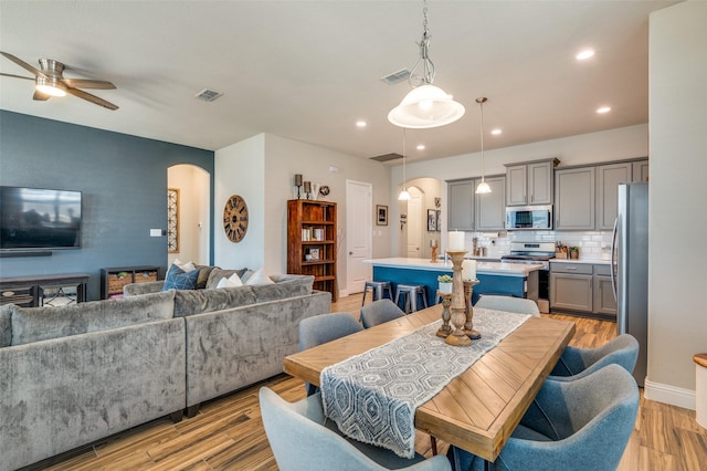 dining space featuring a ceiling fan, light wood-style floors, visible vents, and arched walkways