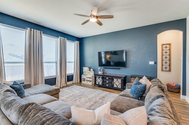 living area featuring arched walkways, baseboards, a ceiling fan, and wood finished floors