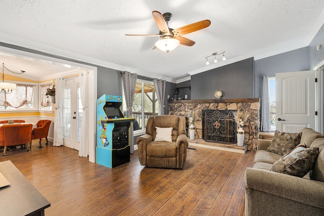 living room featuring ceiling fan with notable chandelier, a stone fireplace, wood finished floors, and ornamental molding