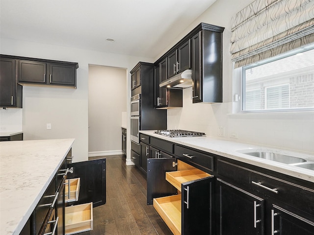 1722 Port Royal Ln, Frisco, TX 75036 - kitchen with under cabinet range hood, stainless steel gas cooktop, dark wood-style floors, dark cabinets, and decorative backsplash