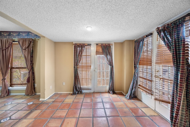 empty room featuring tile patterned floors, a textured ceiling, and baseboards