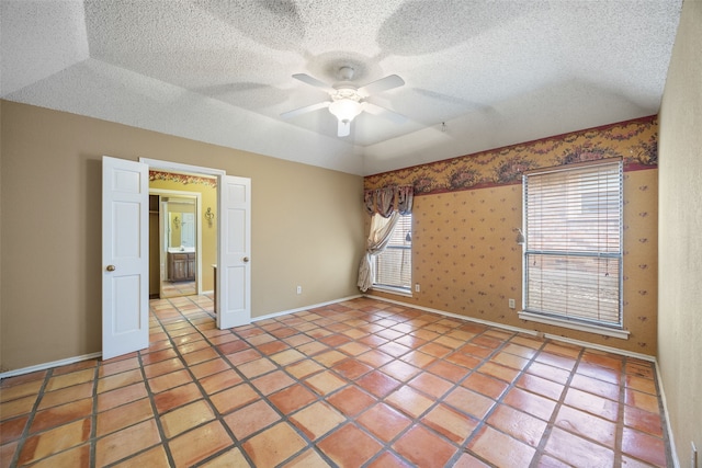 tiled empty room featuring baseboards, a textured ceiling, ceiling fan, and wallpapered walls