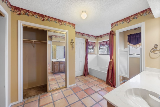 full bathroom with double vanity, a sink, a textured ceiling, a garden tub, and tile patterned floors
