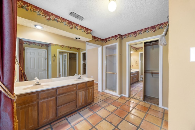bathroom featuring visible vents, double vanity, a stall shower, a textured ceiling, and a sink