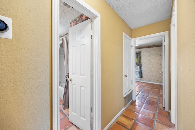 hall featuring visible vents, baseboards, a textured ceiling, and tile patterned flooring