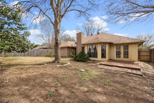 rear view of property featuring a shingled roof, french doors, fence, and a chimney