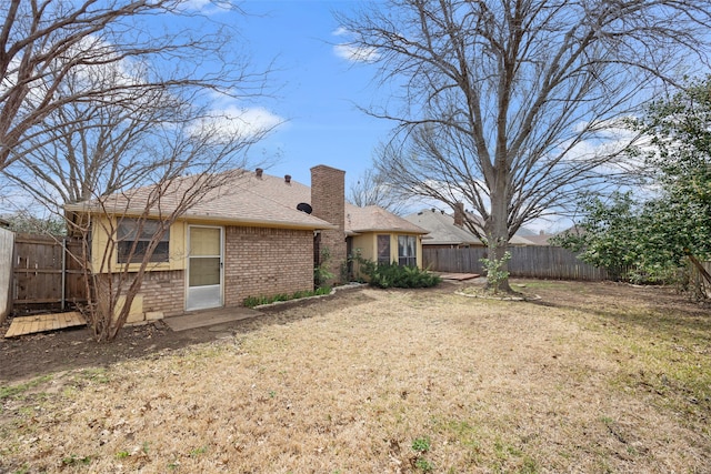 rear view of property with a yard, a fenced backyard, brick siding, and a chimney