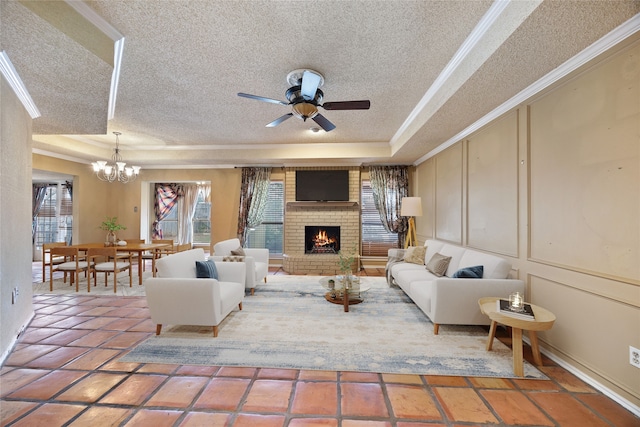 living room with a tray ceiling, a textured ceiling, crown molding, a decorative wall, and a brick fireplace