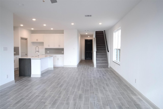 kitchen featuring visible vents, a sink, light countertops, white cabinets, and open floor plan