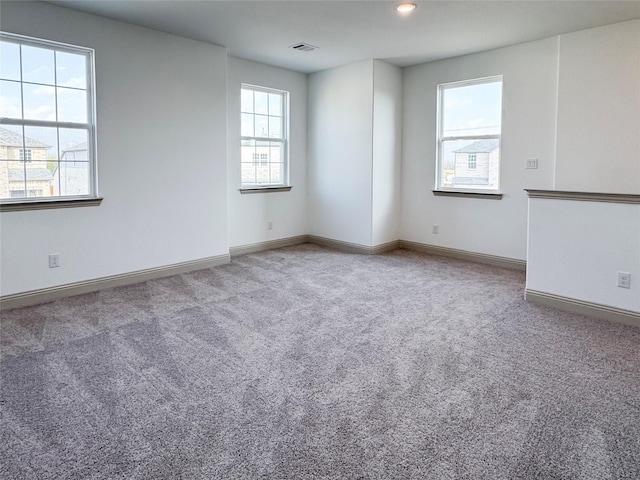 spare room with a wealth of natural light, carpet flooring, baseboards, and visible vents