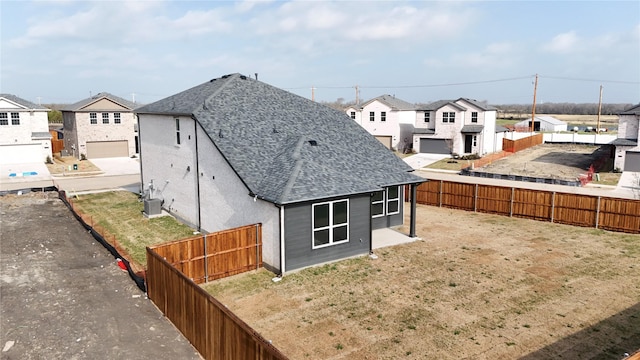 rear view of house featuring a fenced backyard, a residential view, central AC unit, and roof with shingles