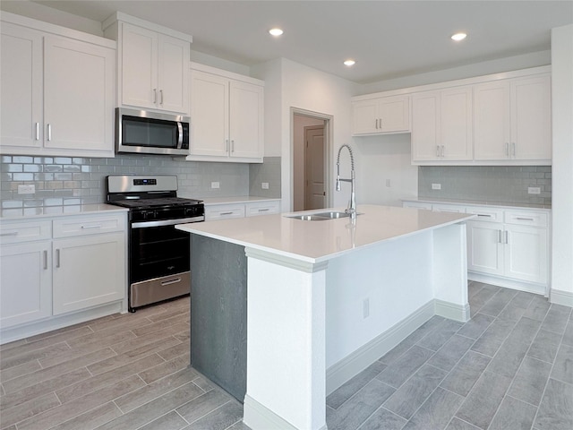 kitchen with a sink, wood tiled floor, light countertops, stainless steel appliances, and a kitchen island with sink