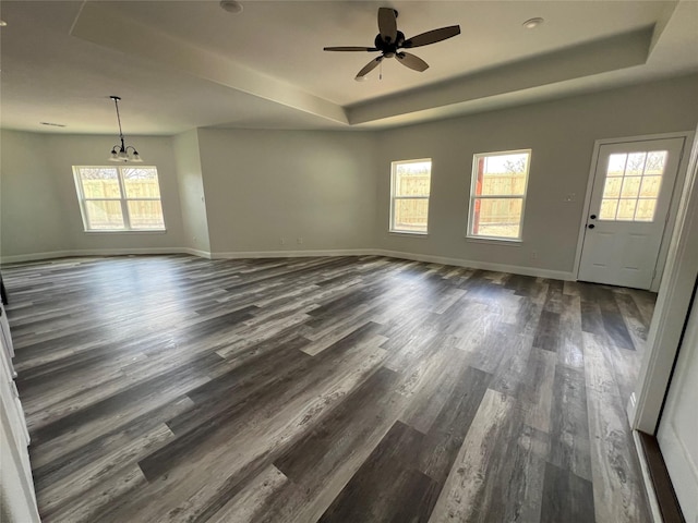 unfurnished living room with a tray ceiling, a wealth of natural light, baseboards, and dark wood-style flooring