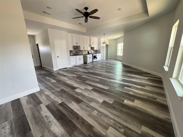 unfurnished living room with dark wood-style floors, a sink, baseboards, visible vents, and a ceiling fan
