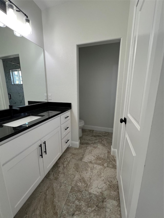 full bathroom featuring stone finish floor, toilet, vanity, baseboards, and walk in shower