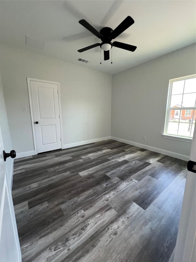 empty room with ceiling fan, visible vents, baseboards, and dark wood-style flooring