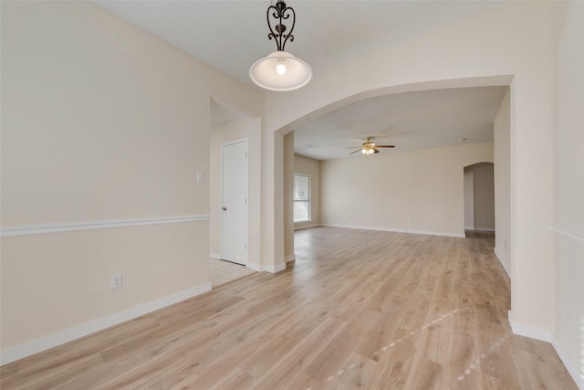 unfurnished room featuring baseboards, arched walkways, a ceiling fan, and light wood finished floors