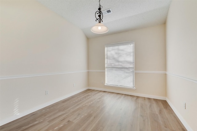 empty room featuring visible vents, a textured ceiling, baseboards, and wood finished floors