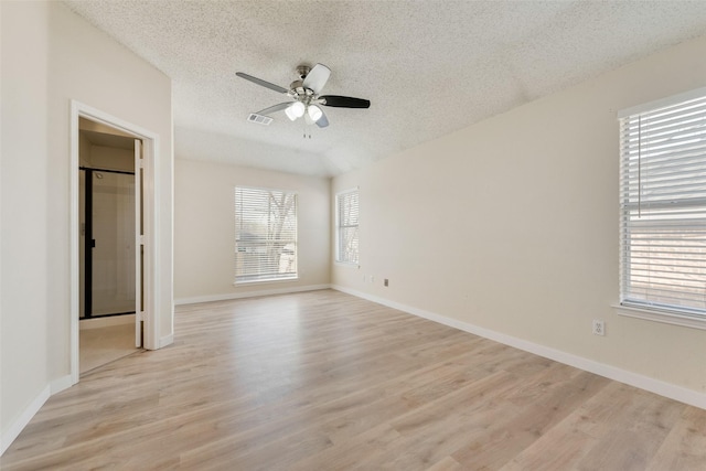 spare room featuring baseboards, a ceiling fan, light wood-style floors, and a textured ceiling