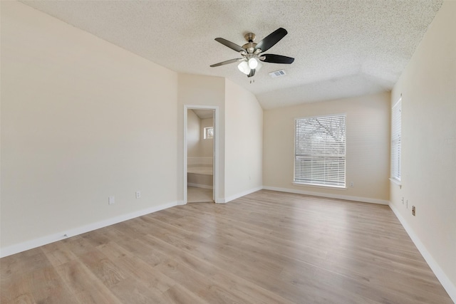 spare room featuring a ceiling fan, visible vents, lofted ceiling, light wood-style flooring, and a textured ceiling