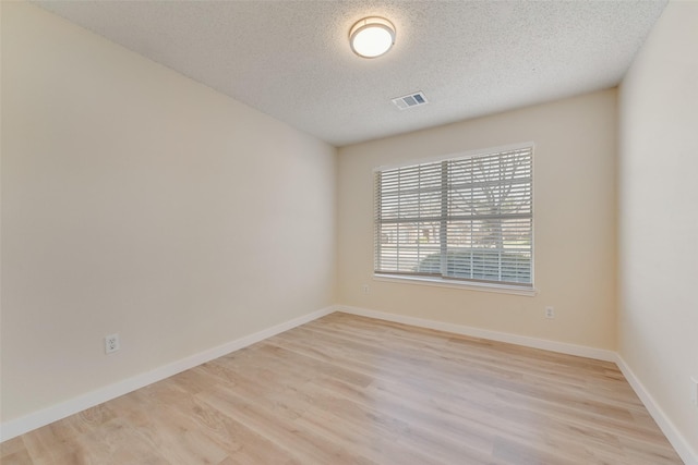 spare room featuring light wood-type flooring, visible vents, baseboards, and a textured ceiling