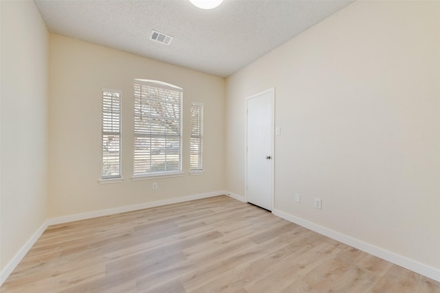 unfurnished room with light wood-type flooring, visible vents, baseboards, and a textured ceiling