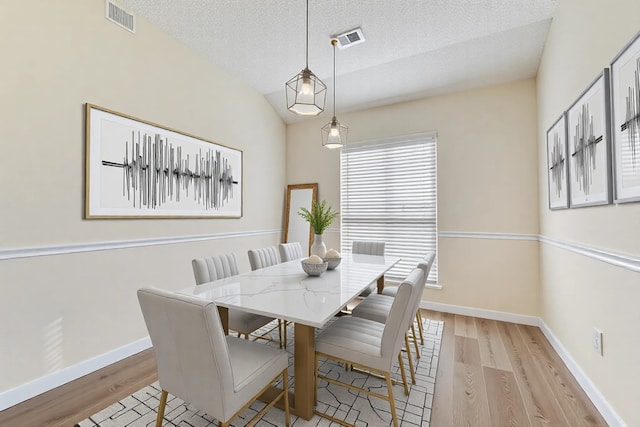 dining space featuring visible vents, baseboards, a textured ceiling, and light wood-style flooring