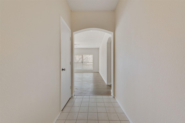 hall with arched walkways, light tile patterned floors, and baseboards