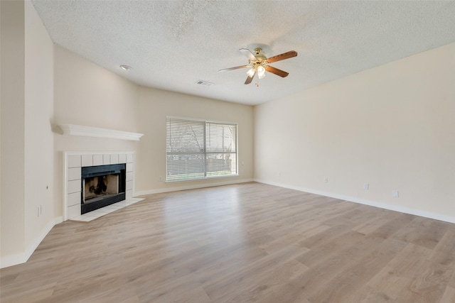 unfurnished living room with visible vents, a textured ceiling, light wood-style floors, ceiling fan, and a tile fireplace