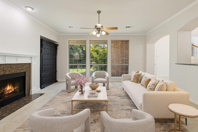 6976 Valley Brook Dr, Frisco, TX 75035 - living area with arched walkways, a ceiling fan, a high end fireplace, ornamental molding, and light tile patterned floors