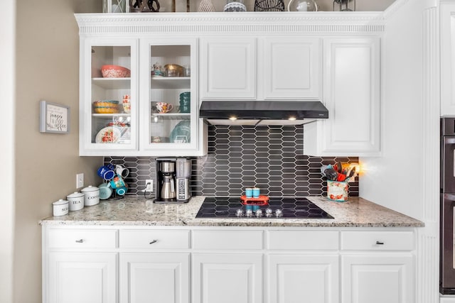 kitchen featuring under cabinet range hood, glass insert cabinets, backsplash, and white cabinets