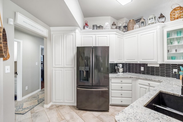 kitchen featuring light stone counters, tasteful backsplash, refrigerator with ice dispenser, and white cabinetry