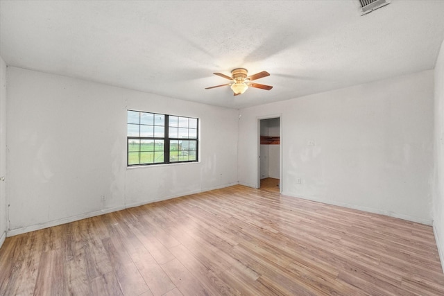 spare room featuring light wood finished floors, visible vents, a ceiling fan, and baseboards