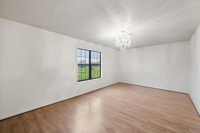 empty room with an inviting chandelier, wood finished floors, visible vents, baseboards, and a textured ceiling