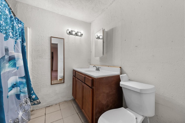 bathroom featuring tile patterned flooring, toilet, a textured wall, and vanity