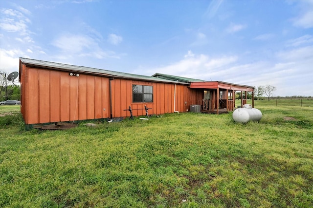 rear view of house with board and batten siding, a yard, and central AC