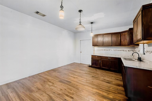 kitchen with light wood finished floors, light countertops, dark brown cabinets, visible vents, and a sink
