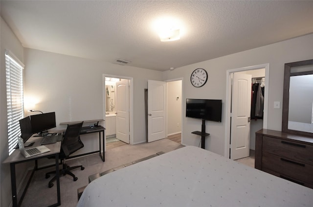 bedroom featuring visible vents, a textured ceiling, a walk in closet, light colored carpet, and connected bathroom