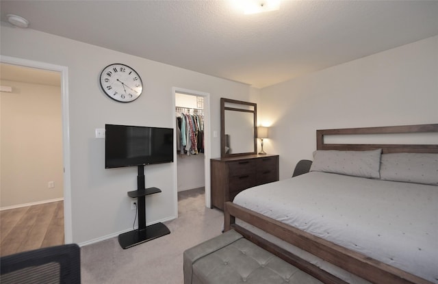 carpeted bedroom with a closet, a textured ceiling, a walk in closet, and baseboards