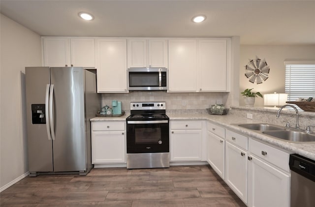 kitchen featuring wood finished floors, a sink, stainless steel appliances, white cabinetry, and backsplash