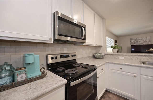 kitchen with electric range, a sink, stainless steel microwave, white cabinets, and decorative backsplash